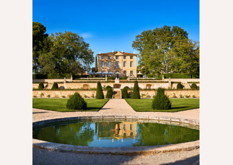 Grande bastide provençale surplombant un jardin à la française avec un bassin d'eau circulaire au premier plan.