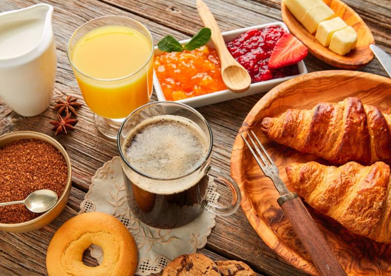 Un petit-déjeuner complet avec café, croissants, jus d'orange et confitures sur une table en bois.