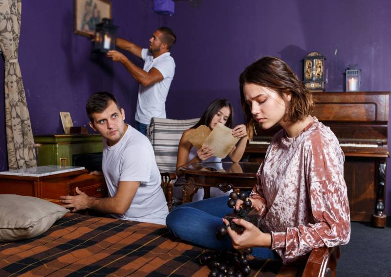 Un groupe d'amis cherchant des indices et résolvant des énigmes dans une salle d'escape game aux murs violets.